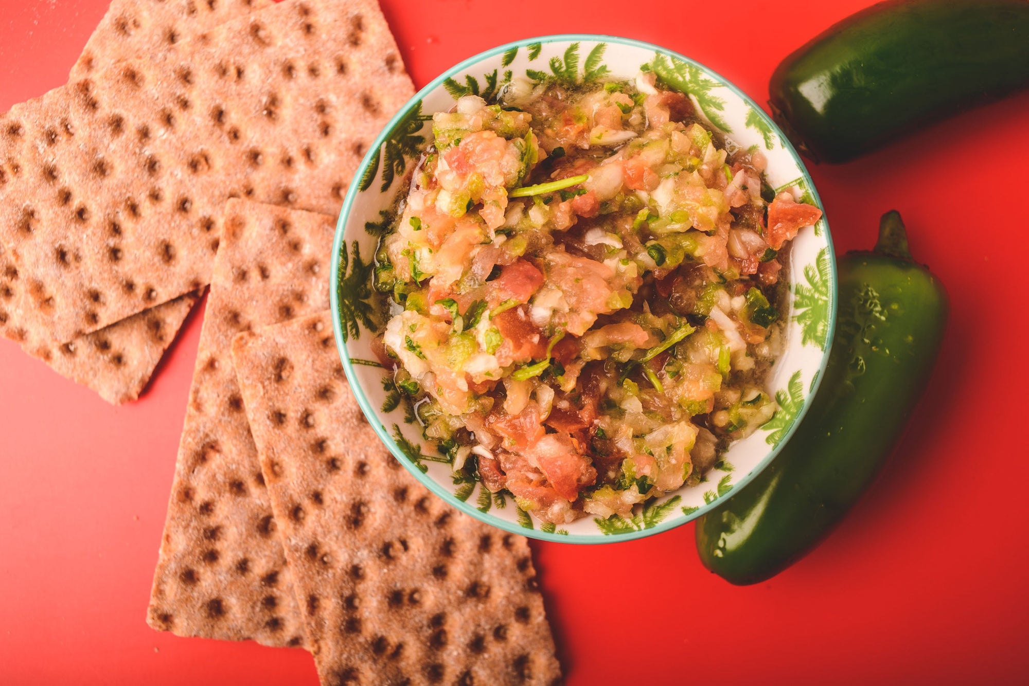 Pico De Gallo in a bowl with crackers and jalapeños